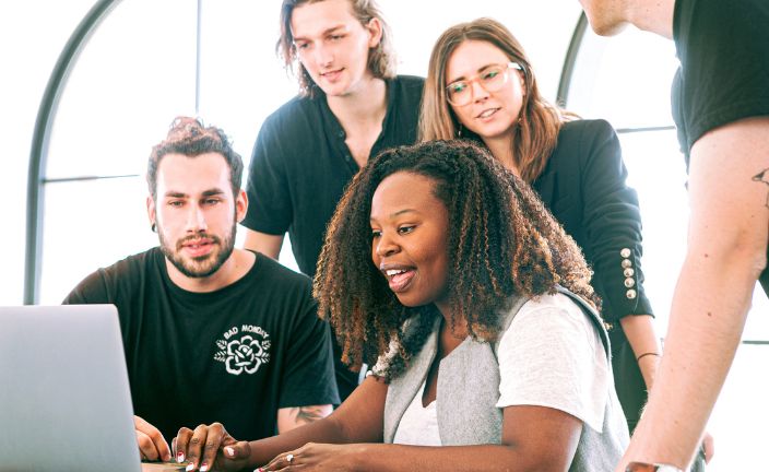 group of people gathered around a woman on a silver laptop.