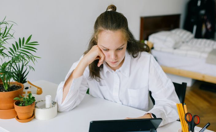 Girl sitting at desk in bedroom using tablet.