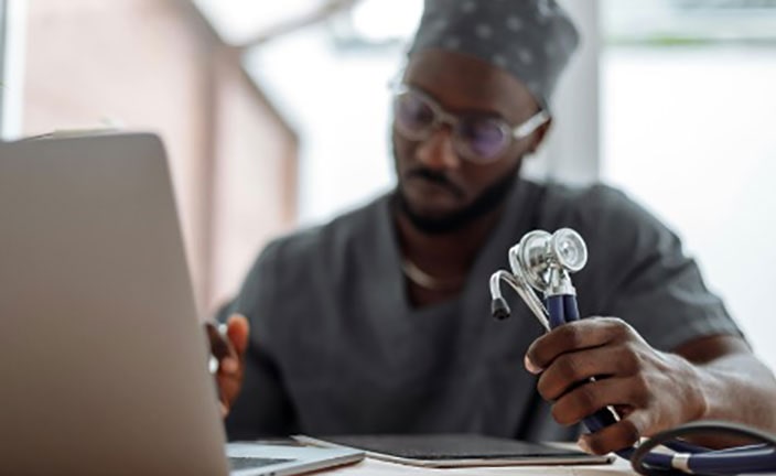 Doctor in scrubs holding a stethoscope on a computer.