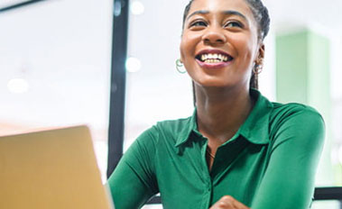 Smiling woman in green shirt sitting in front of laptop in an office.