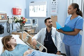 Doctor and medical assistant with patient in hospital room.