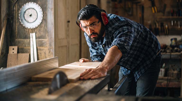 carpenter using table saw in workshop.