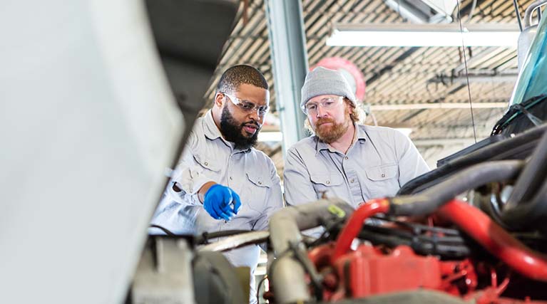two mechanics inspect truck engine.
