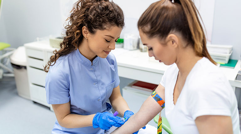 phlebotomist drawing blood from patient in exam room.