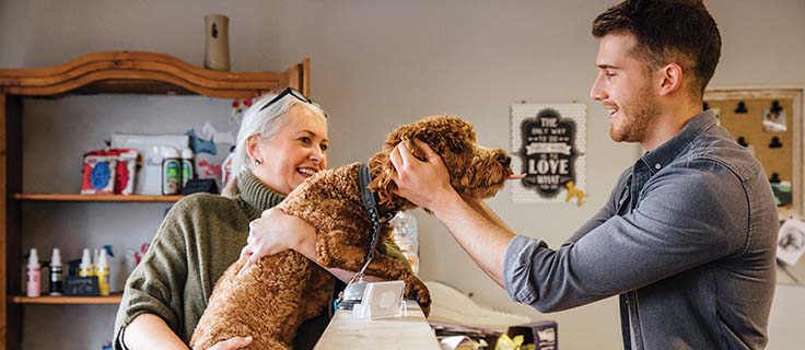 man petting a dog at front desk in a lobby.